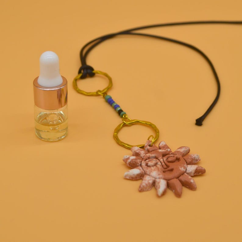 Sun pendant on a black cord next to a dropper bottle